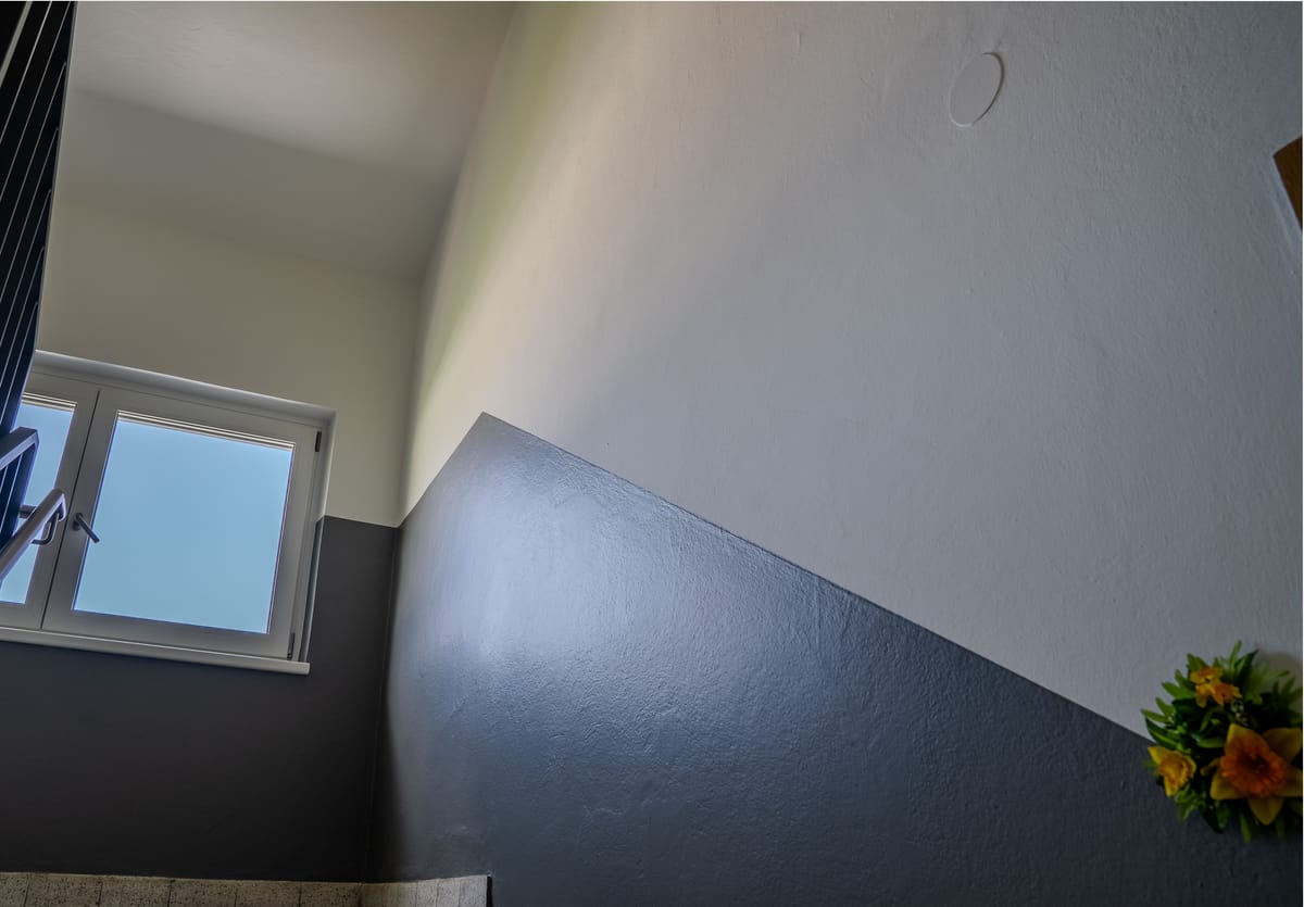 Saniertes Stiegenhaus mit weißer Wand und anthrazitfarbenem Sockel